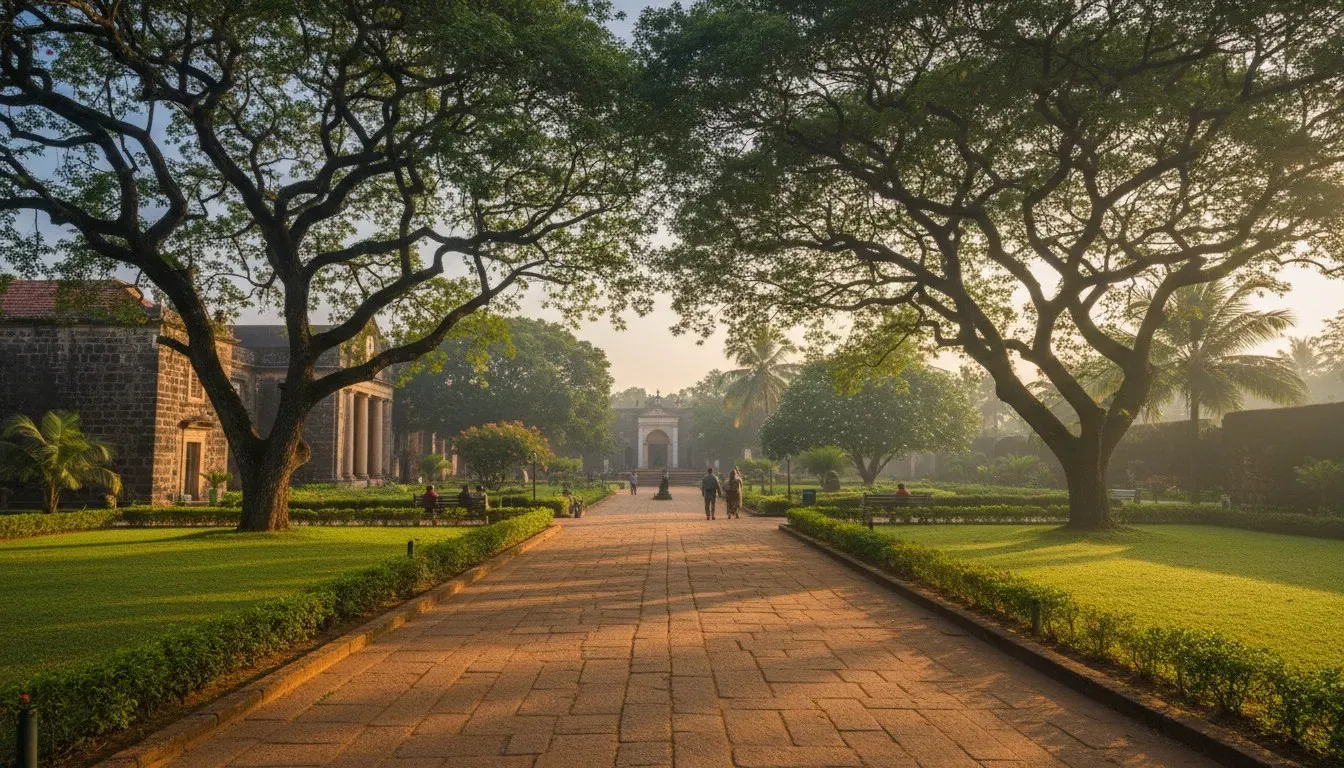 Broad stone walkway through manicured green lawns and mature shade trees in a historic Goan church complex.