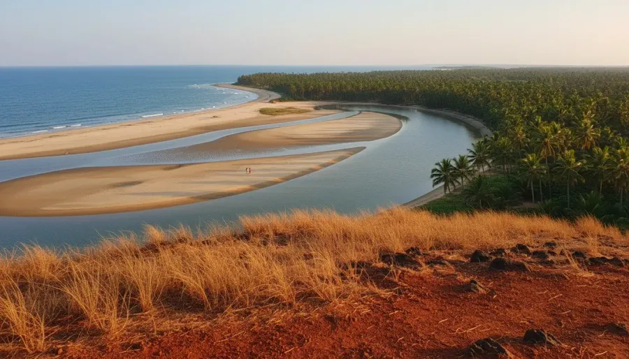 Elevated view of the sandy river mouth and ocean sandbars framed by red laterite terrain in warm afternoon light.